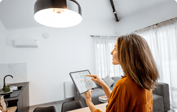 women in her home holding tablet with controls to her home as she smiles and looks at the room's overhead light