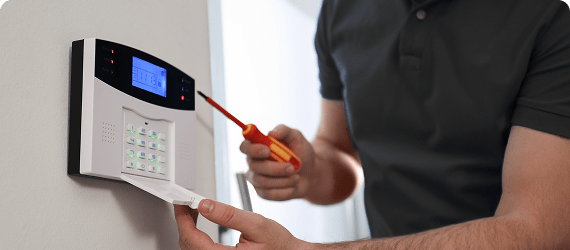 man holding screwdriver near home security controls box on a wall