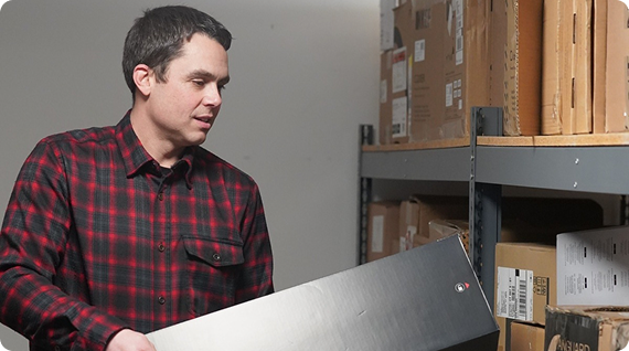 man putting a black cardboard box with a "Sonos" logo onto a shelf with other cardboard boxes