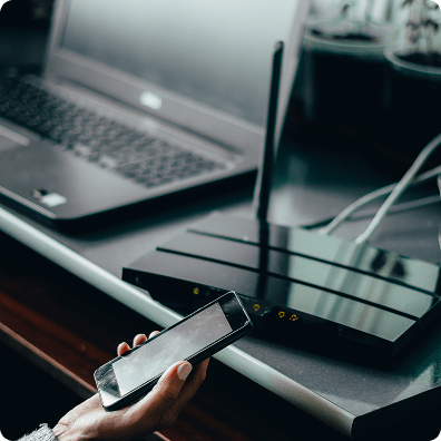 hand holding a smartphone near a router and laptop